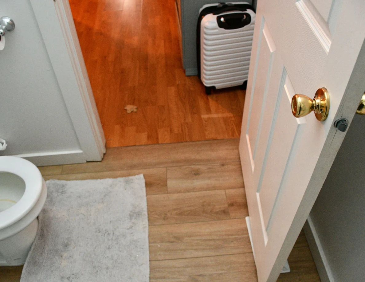 Bathroom doorway with suitcase visible on the landing outside.