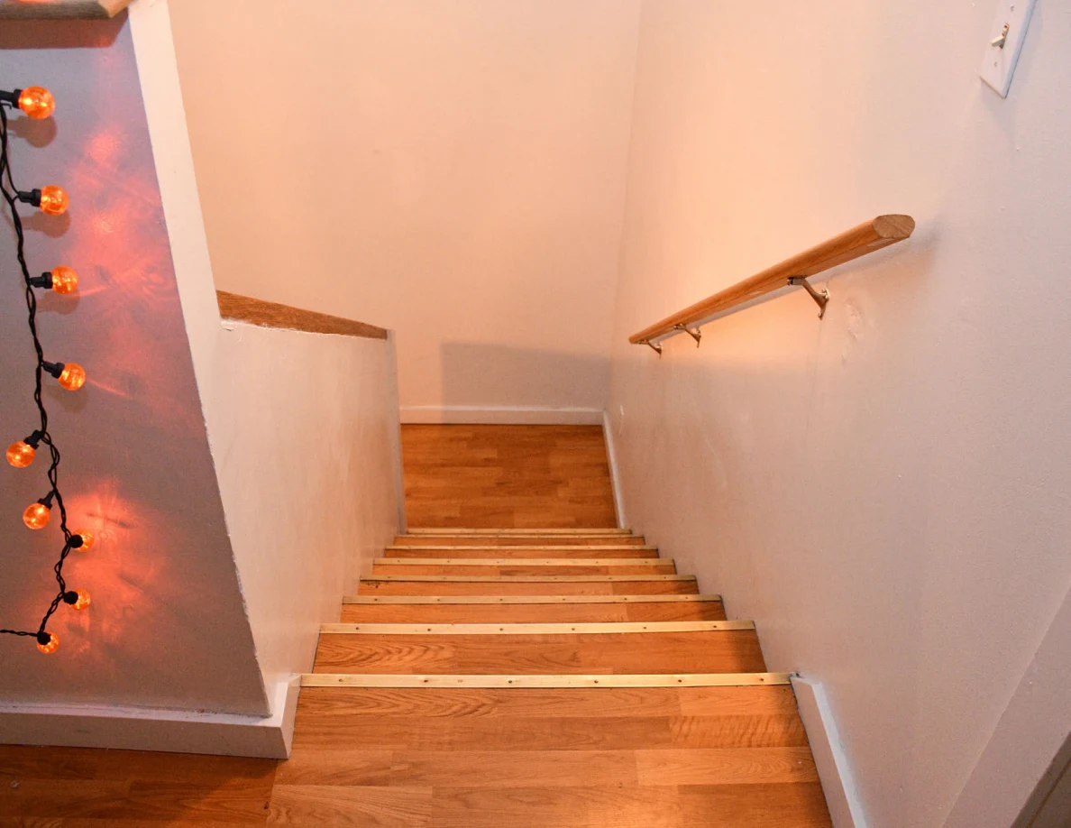 View down a wooden staircase beside orange string lights.
