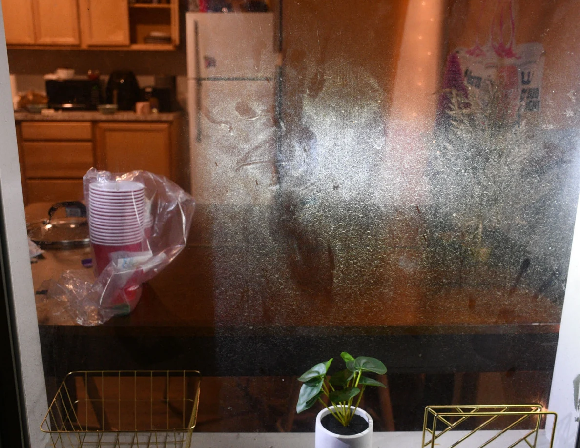Smudged window glass with kitchen cabinets and refrigerator visible behind.