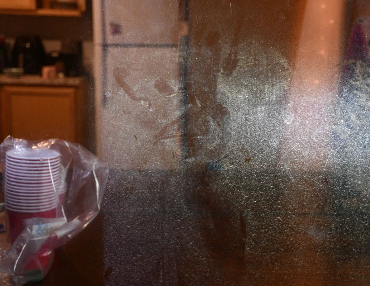 Close view of smears on glass with stacked cups and kitchen behind.