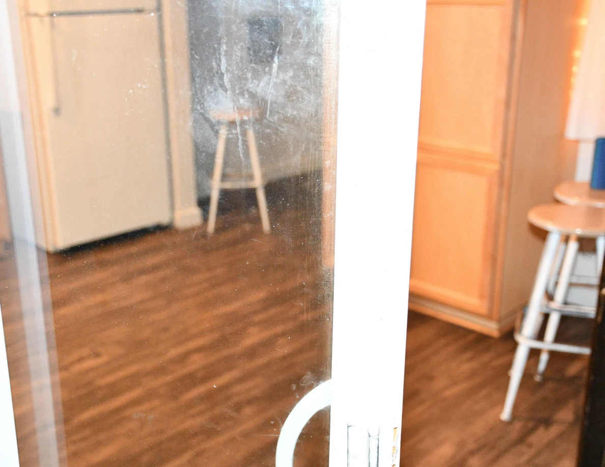 Sliding glass door with kitchen cabinets and stools visible through it.