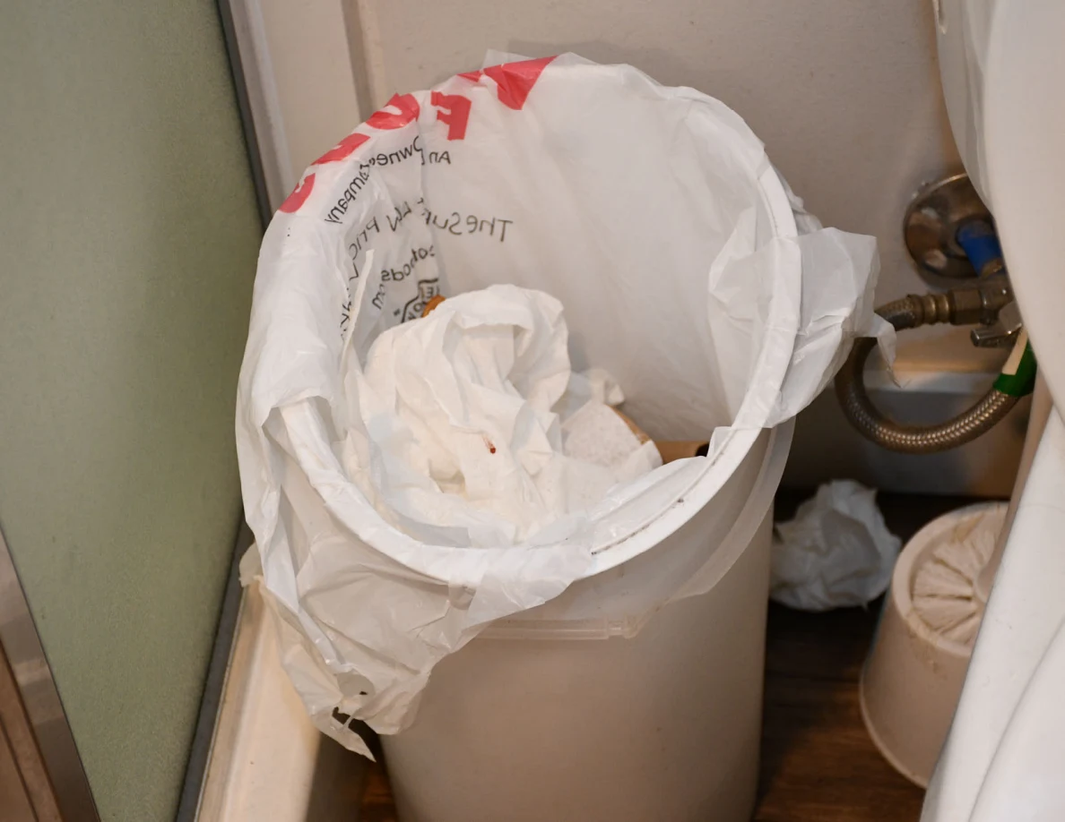 Bathroom trash bin containing crumpled white paper.