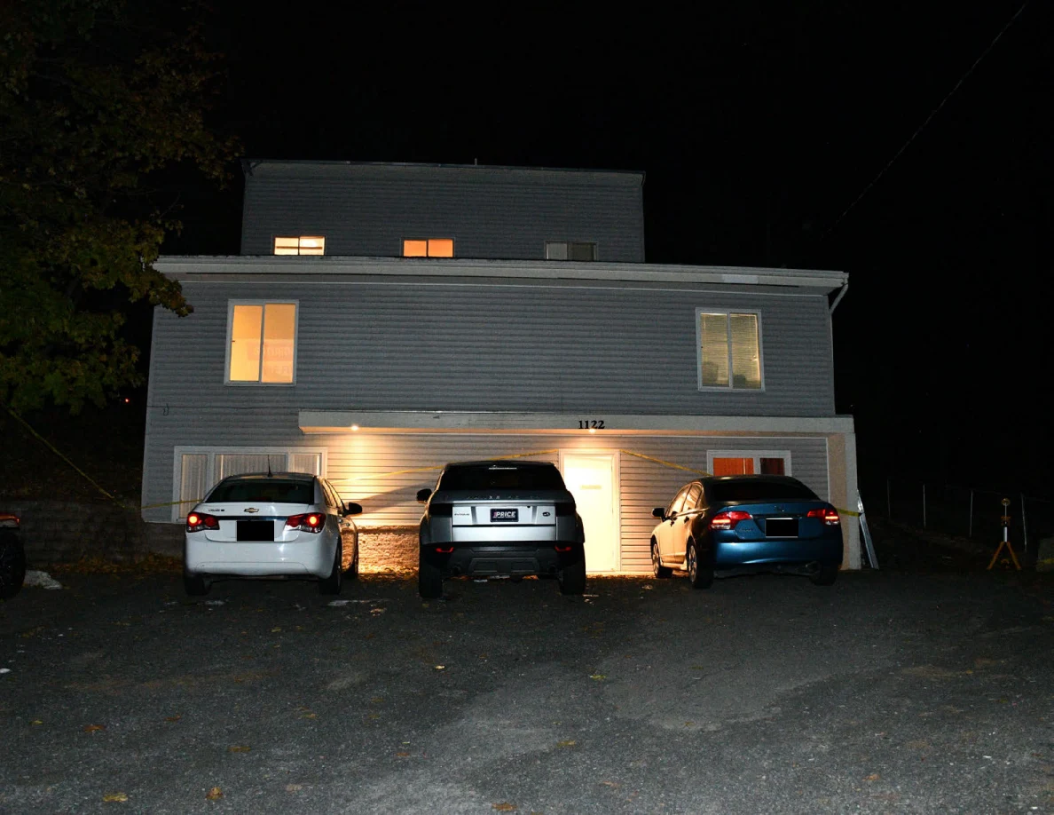 House exterior at night with three parked cars and lit windows.