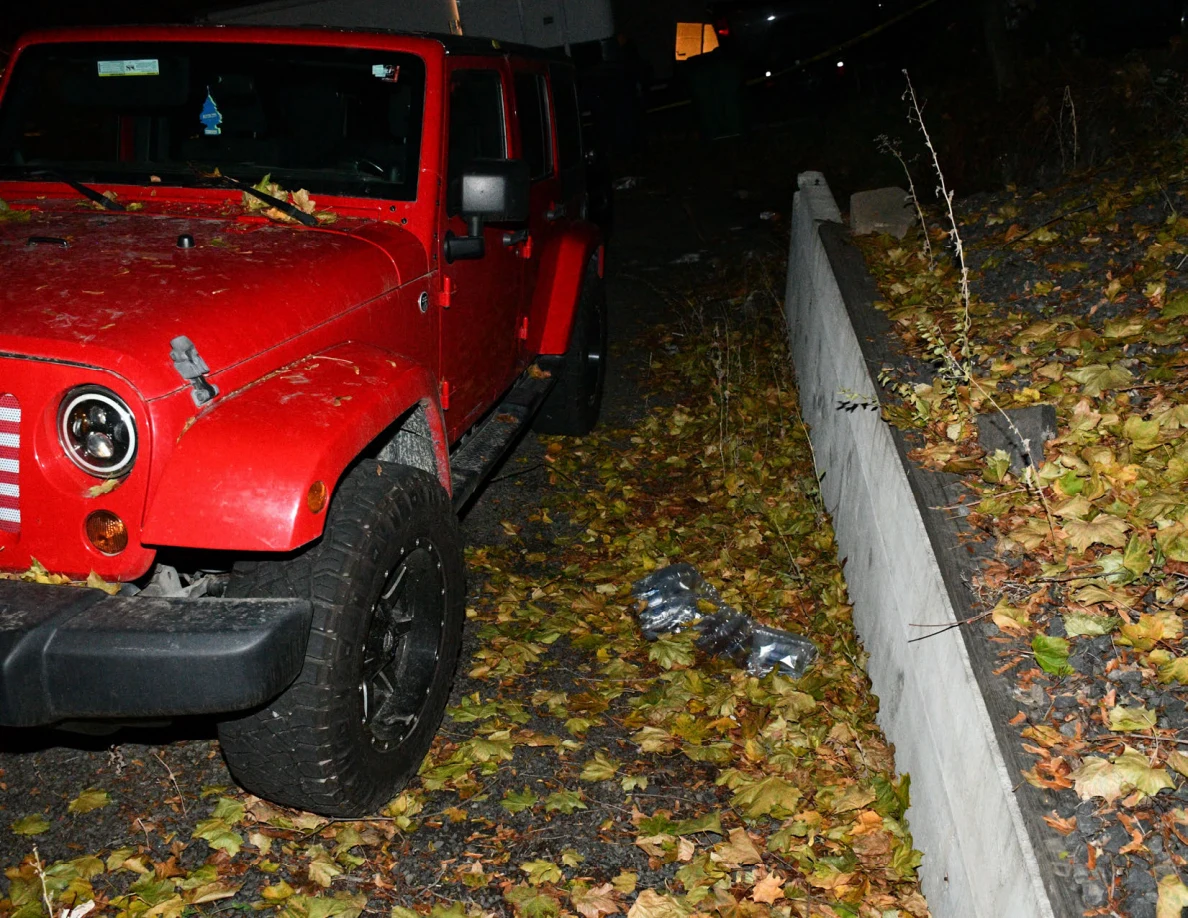 Red Jeep beside a low retaining wall and fallen leaves.