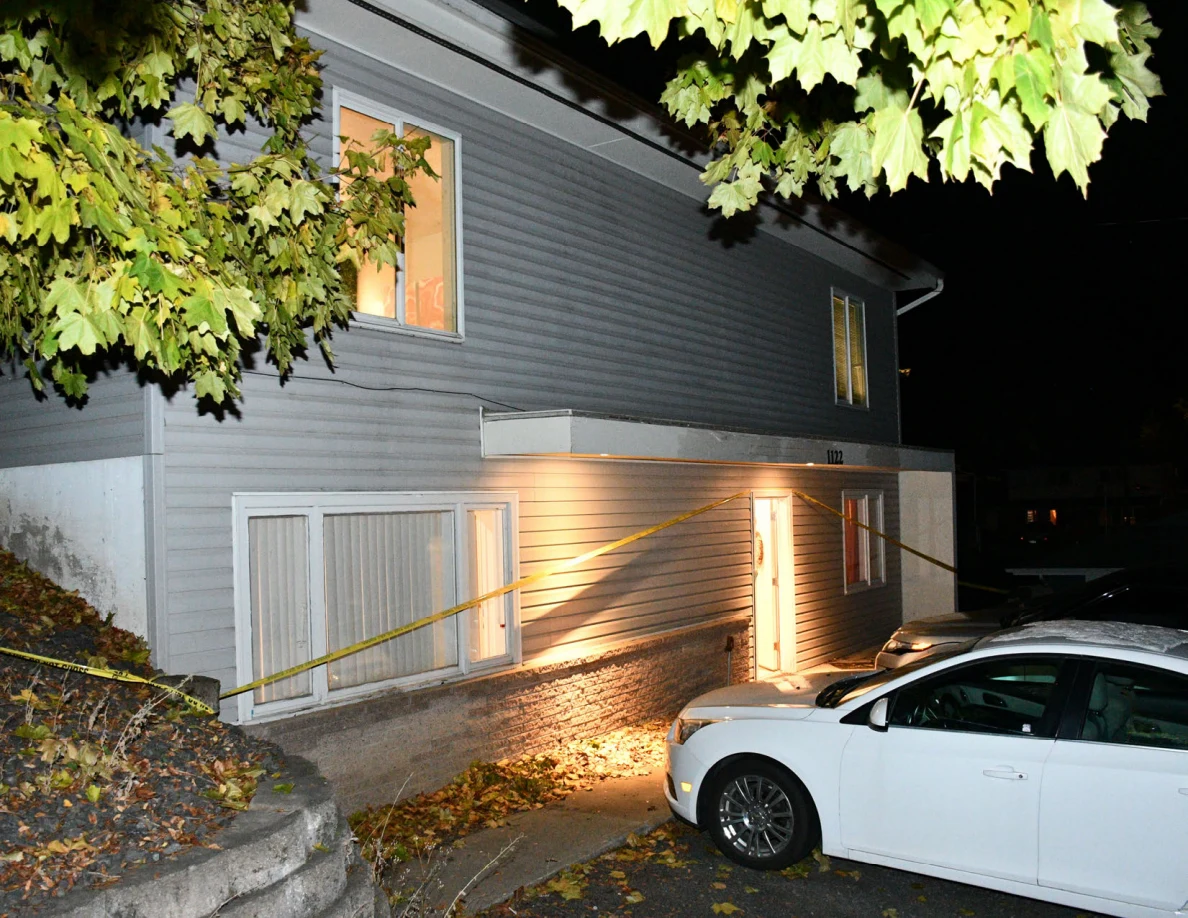 House exterior and white car beneath tree branches and yellow barrier tape.