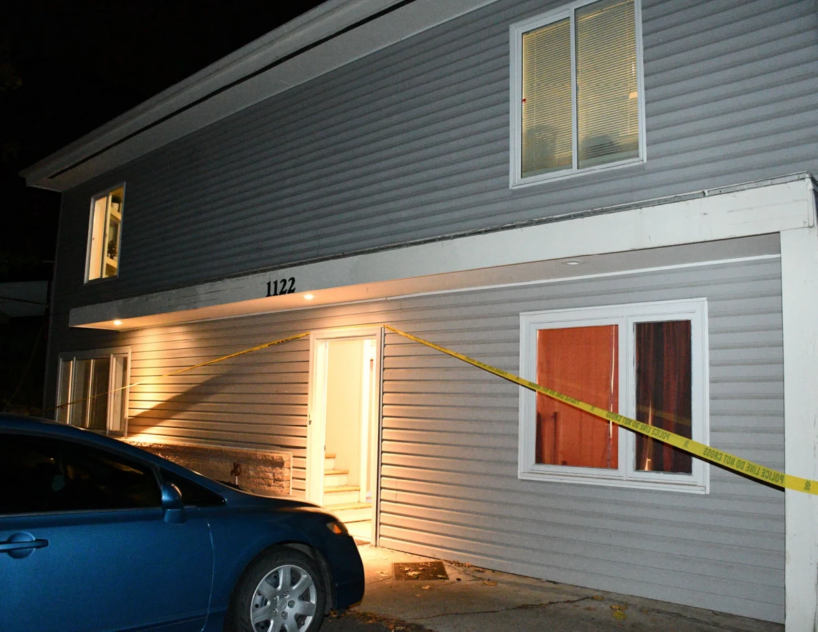House entrance and windows behind a blue car and yellow barrier tape.