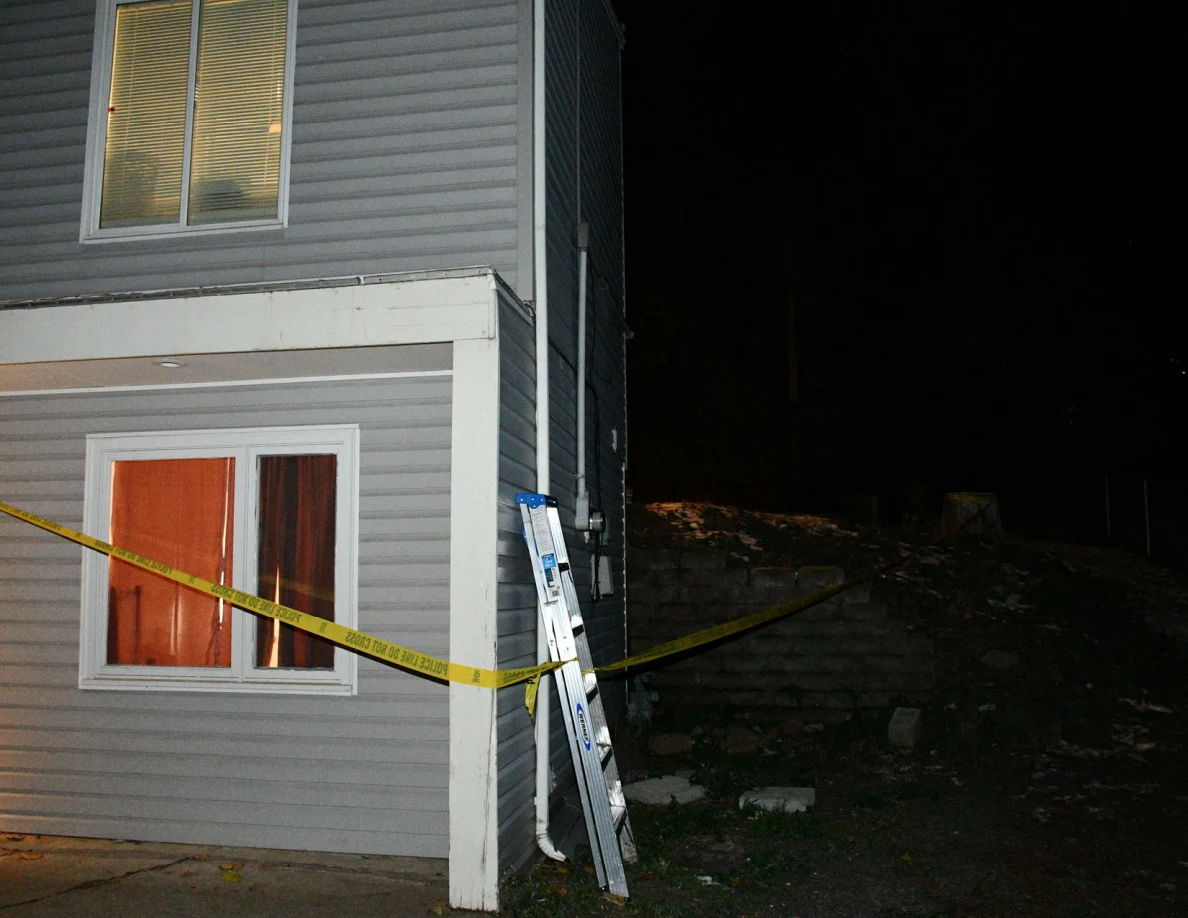 House corner, windows and ladder beside yellow barrier tape.