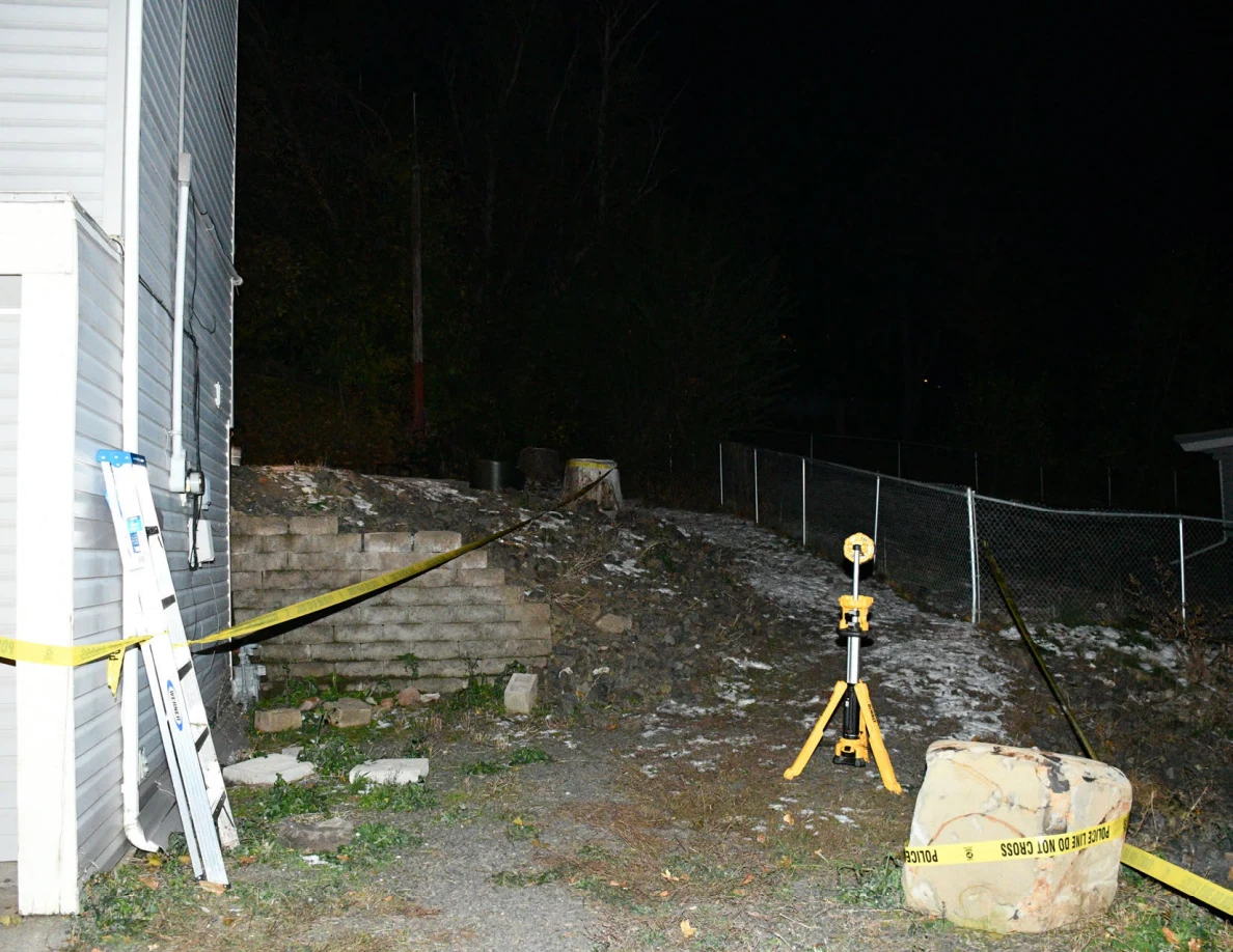 Ladder and yellow tripod on sloping ground beside house and fence.