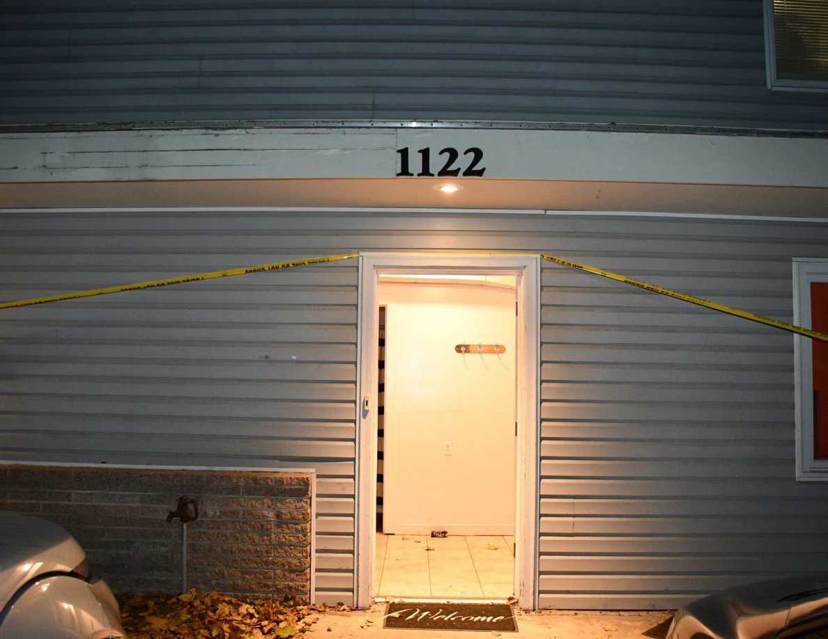 Open front doorway beneath house number 1122 and yellow barrier tape.