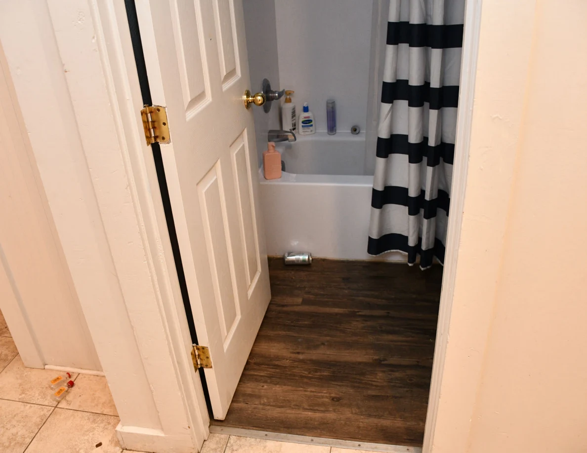 Bathroom doorway showing bathtub, toiletries and striped shower curtain.
