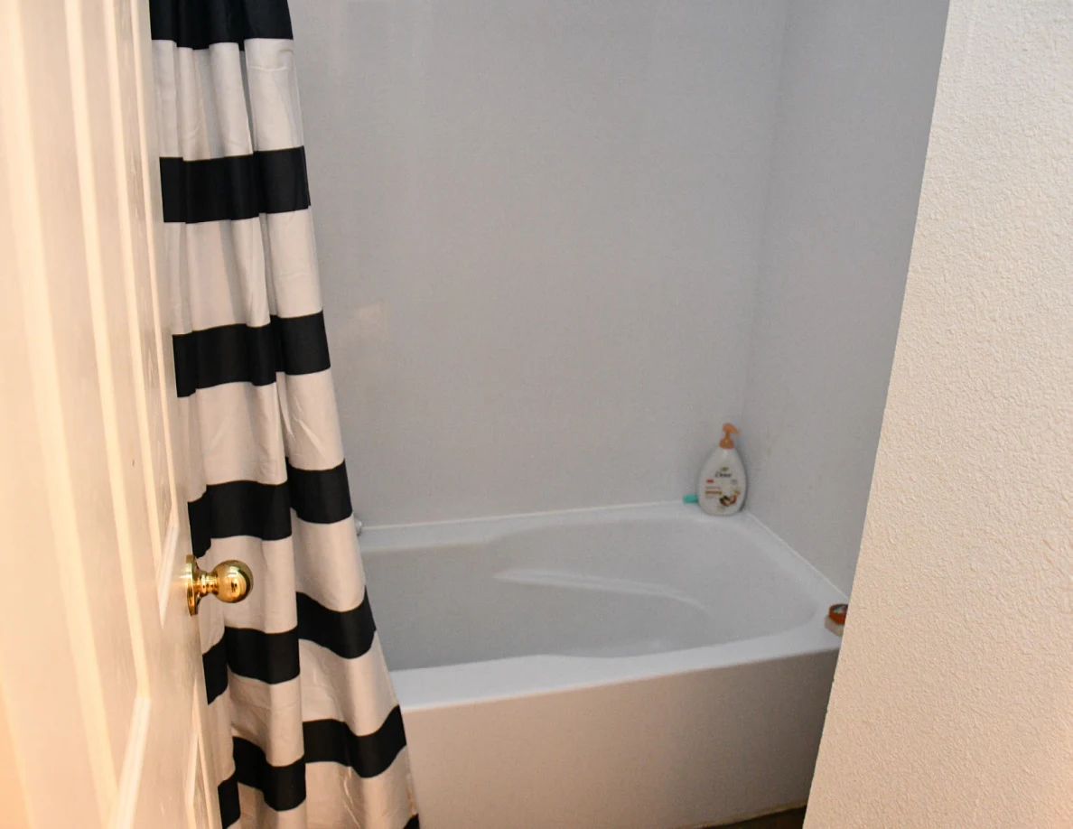 Bathtub with striped shower curtain and bottle on the edge.