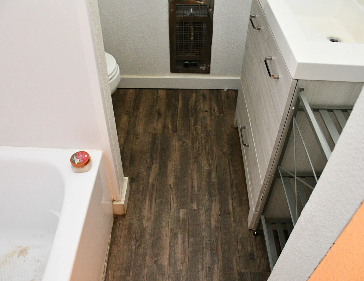 Bathroom floor, vanity cabinet, wall heater and bathtub edge.
