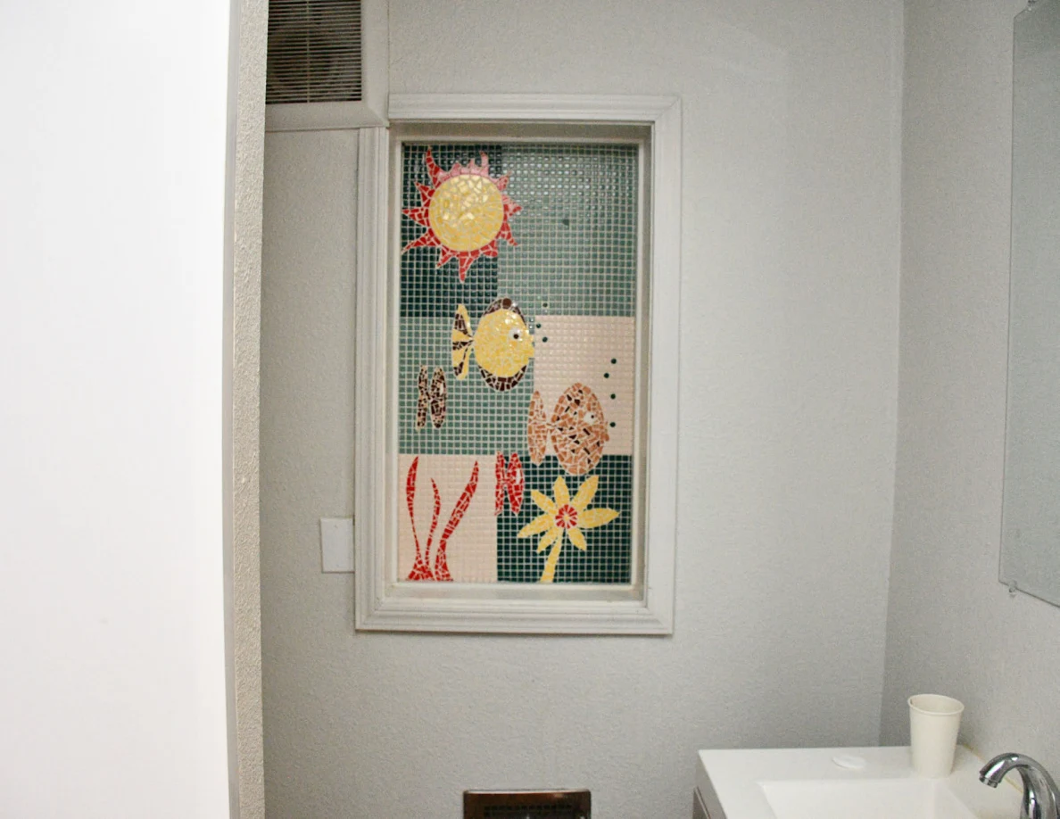 Bathroom window with colorful flower artwork and sink edge.