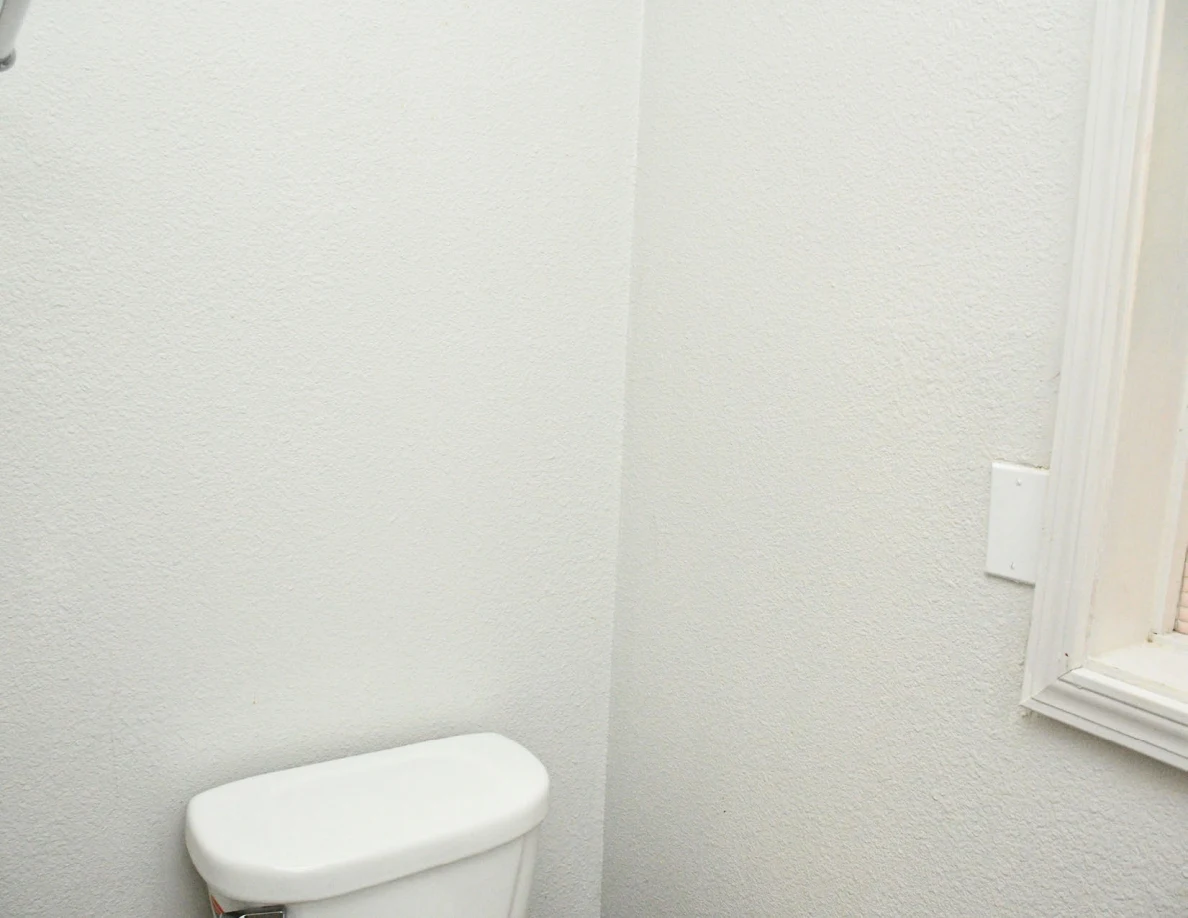 Bathroom wall above toilet tank beside window frame.