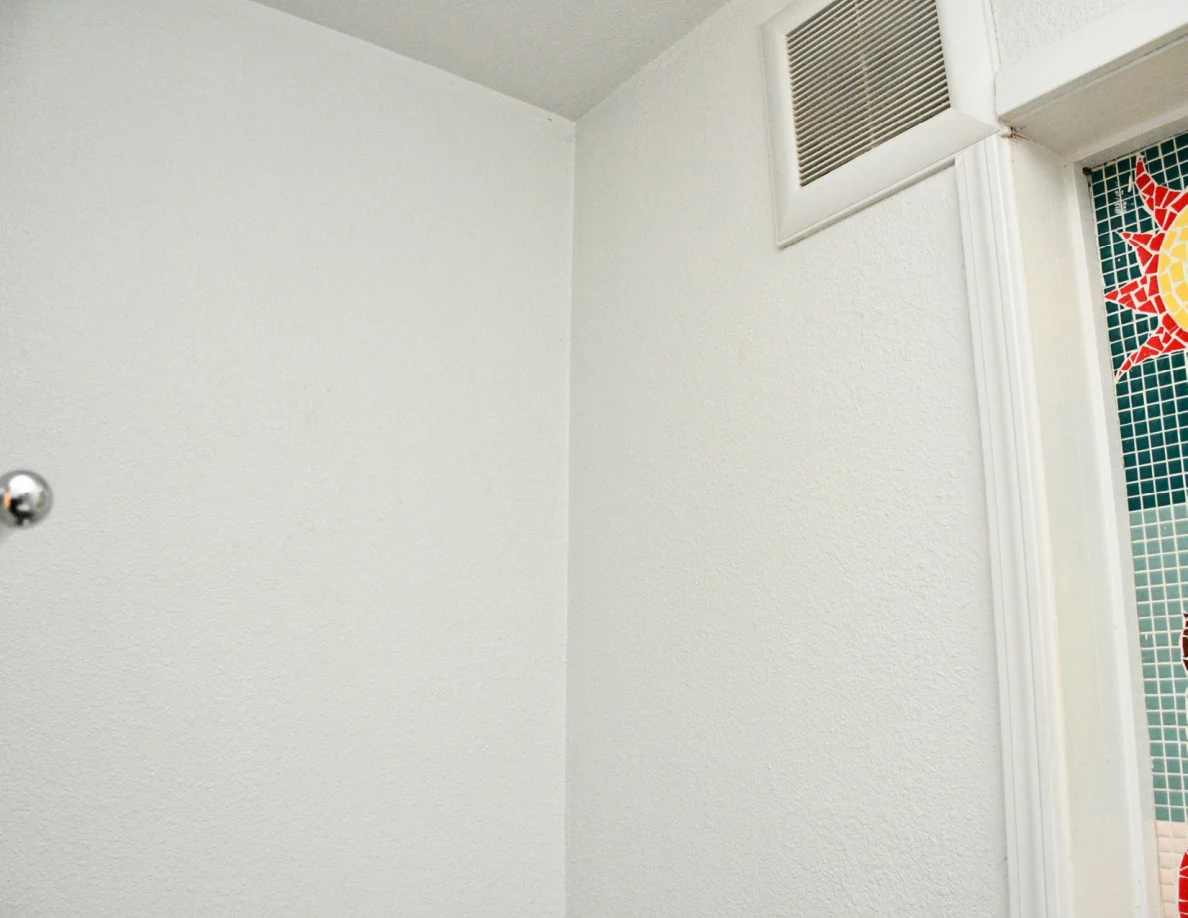 Upper bathroom wall and vent beside decorated window.