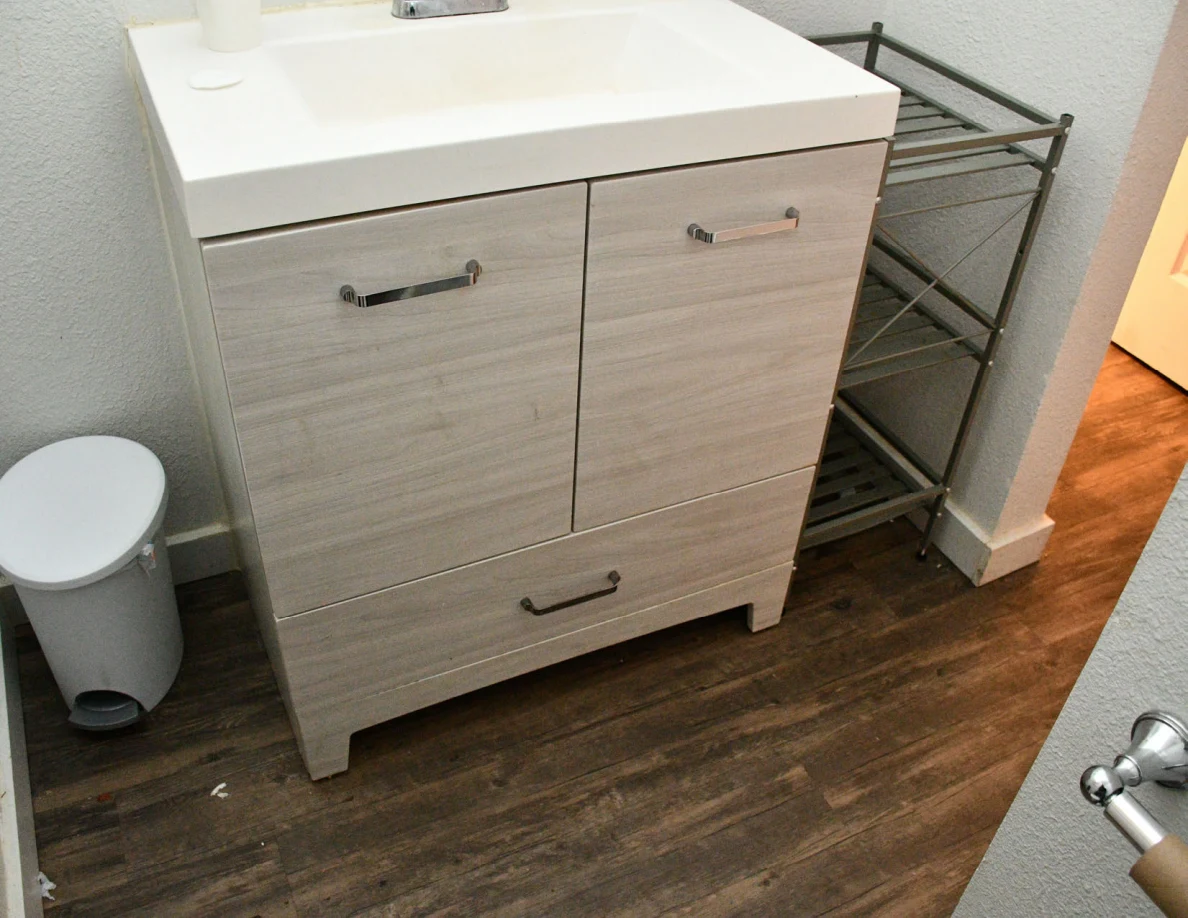 Bathroom vanity cabinet, metal shelving and small trash bin.