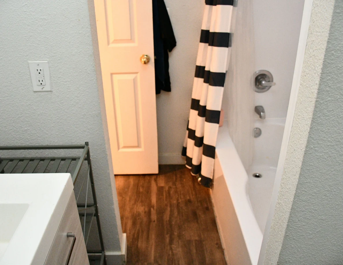 Bathroom doorway, striped shower curtain, bathtub and wood-pattern floor.