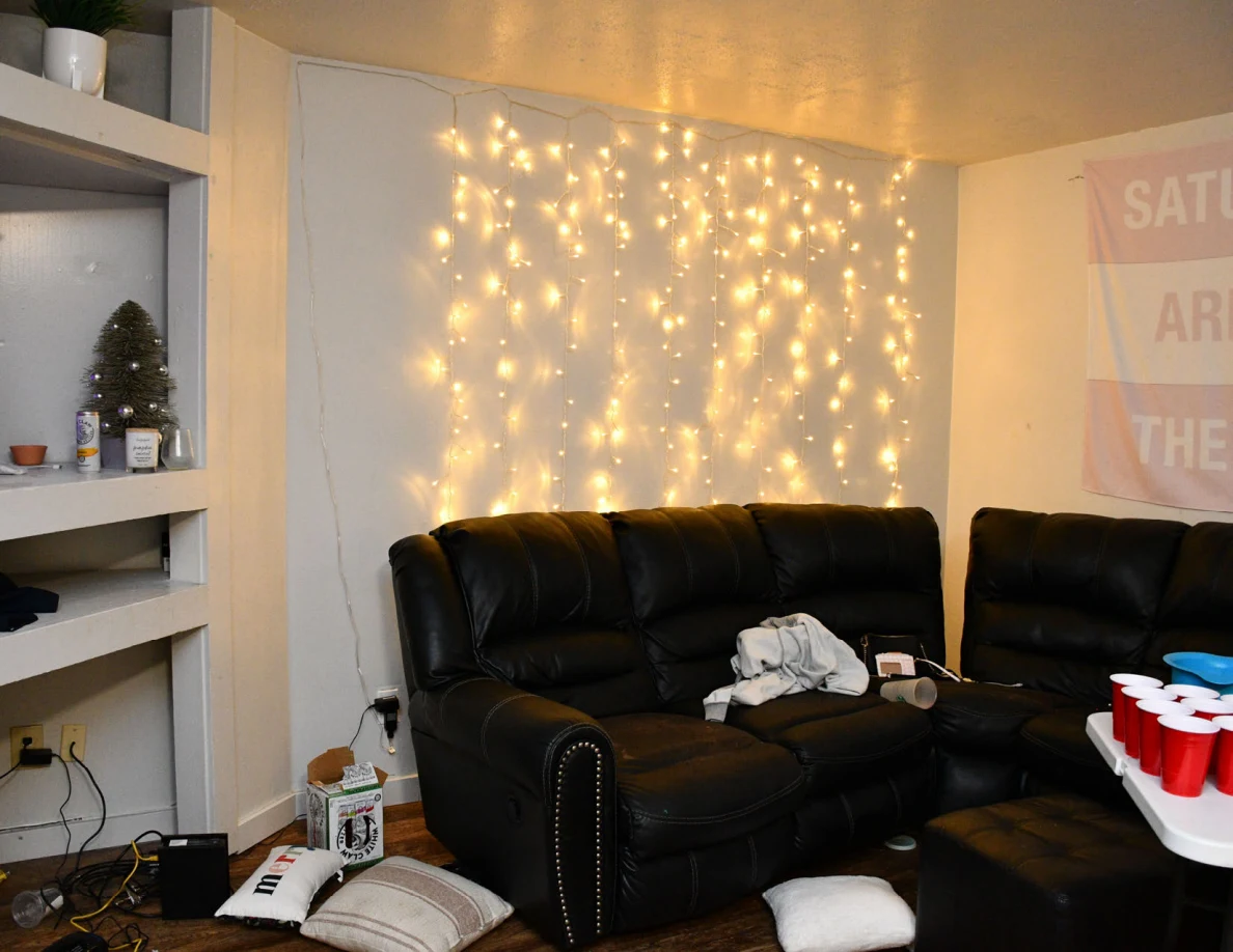 Living room sofa beneath string lights with red cups on folding table.