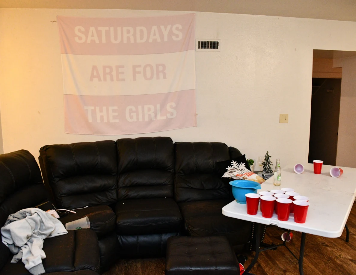Black sectional sofa below wall banner beside folding table with red cups.