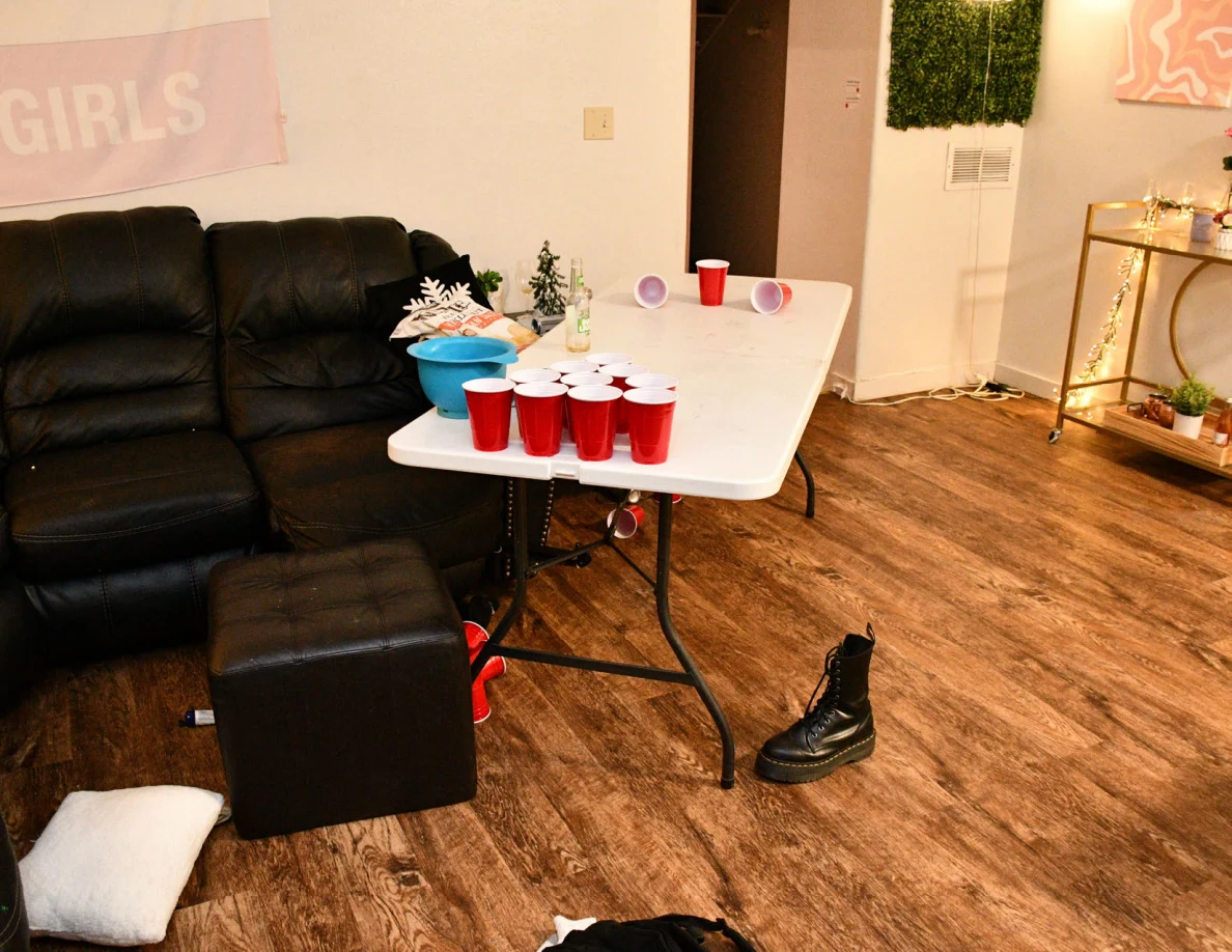 Folding table with red cups beside sofa and a black boot on floor.