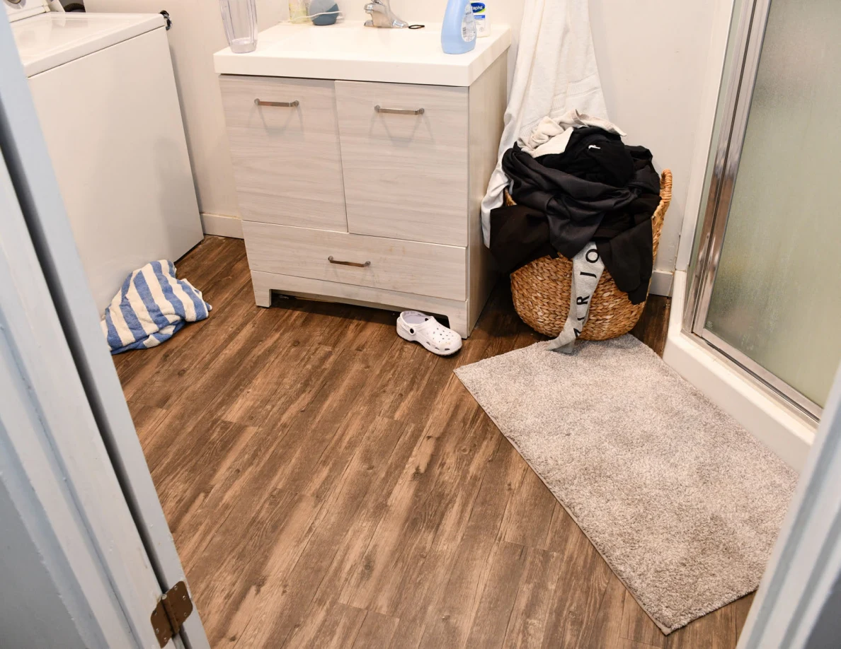 Bathroom floor beside vanity, laundry basket, footwear and shower mat.