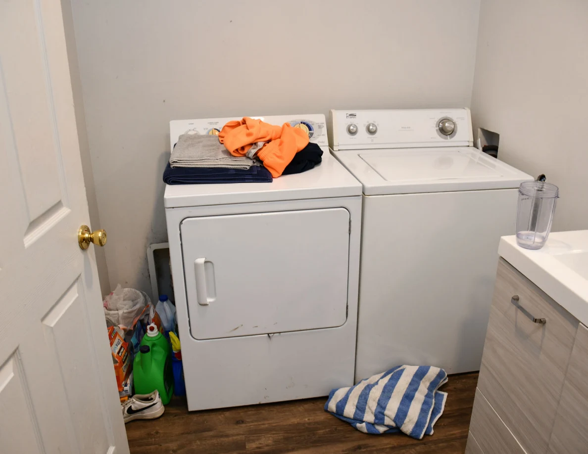 Washer and dryer with folded clothing and striped towel on floor.