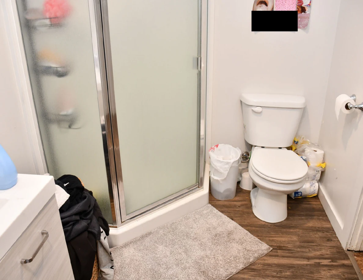 Toilet, lined trash bin and shower mat beside glass shower enclosure.