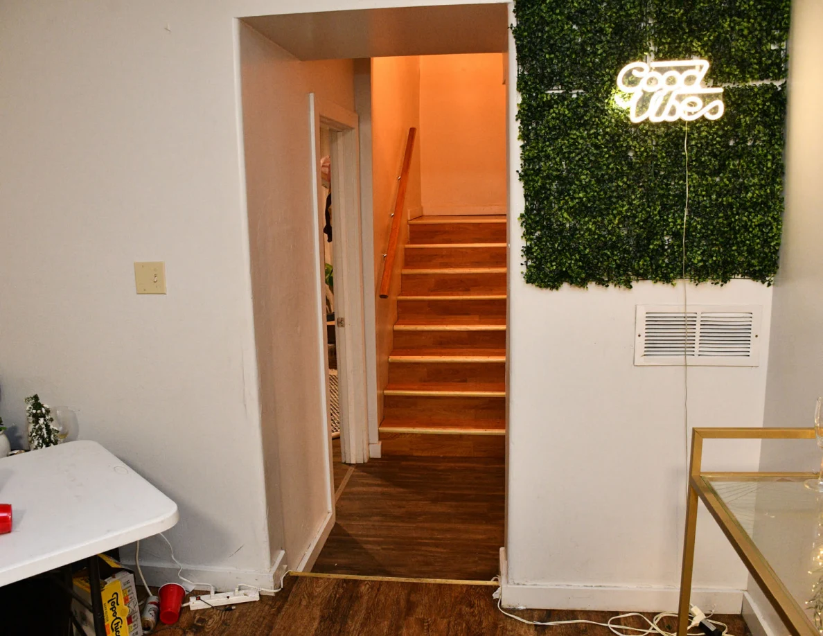 Hallway and stairs beside foliage panel with illuminated Good Vibes sign.