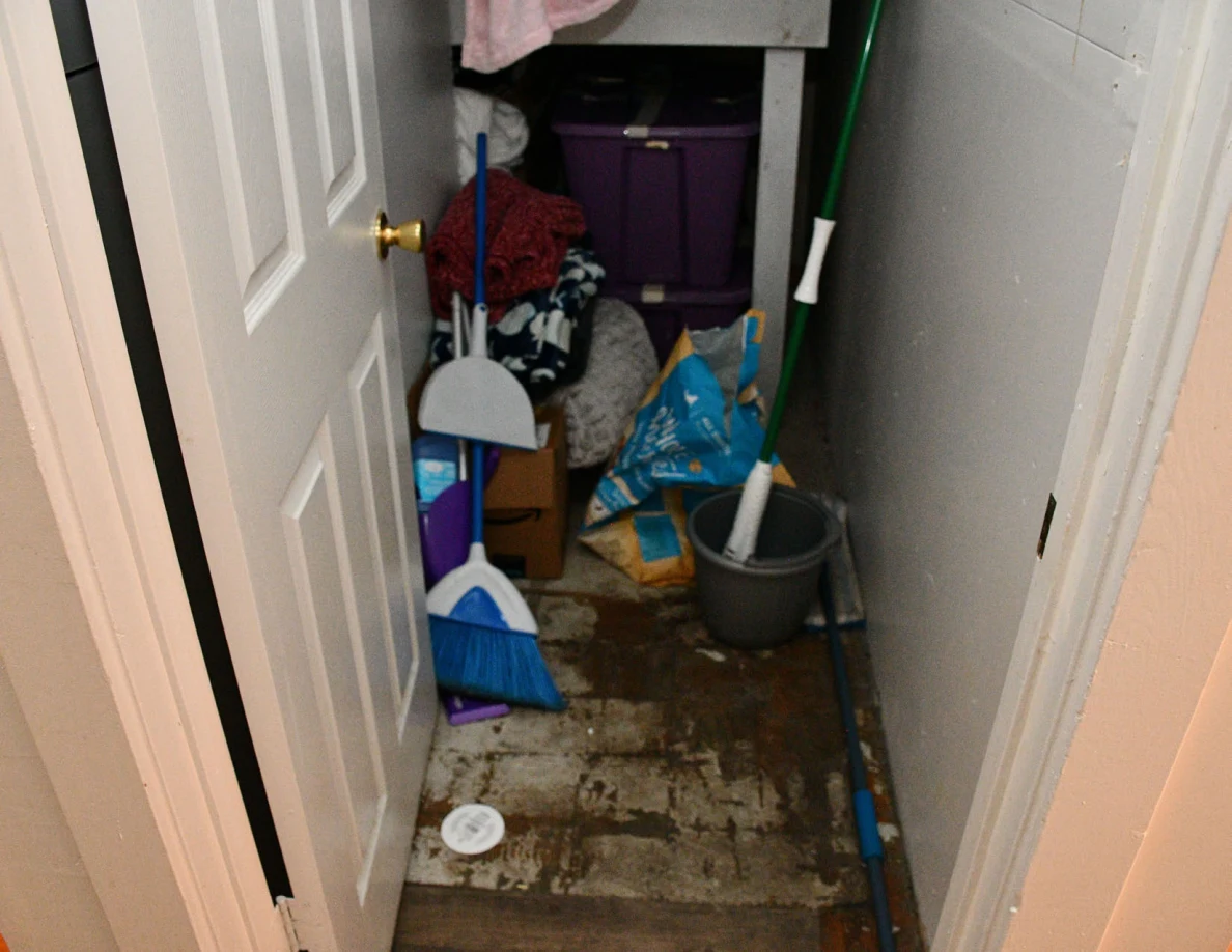 Cupboard floor with cleaning equipment, bucket and stored household items.