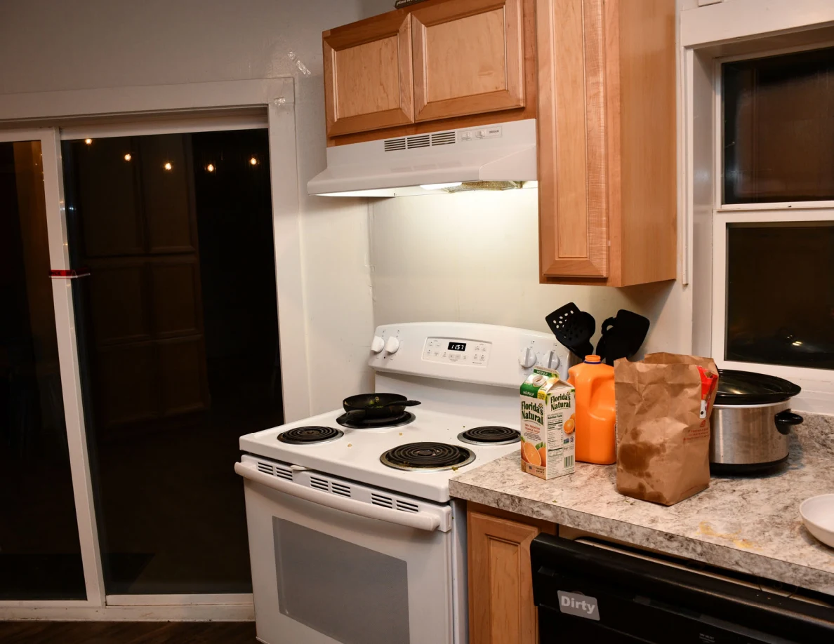 Electric stove and range hood beside countertop with utensils and paper bag.