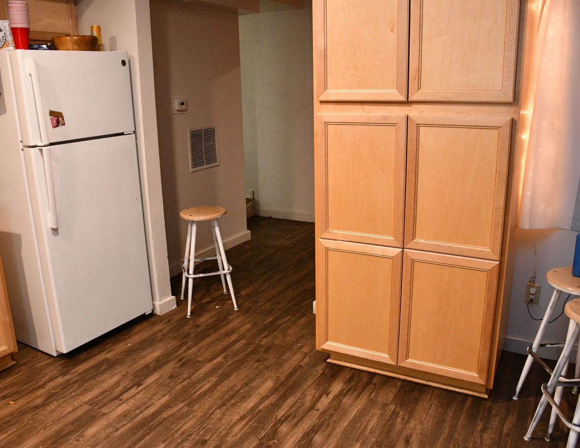 Kitchen refrigerator, tall cabinet, stools and wood-pattern floor.