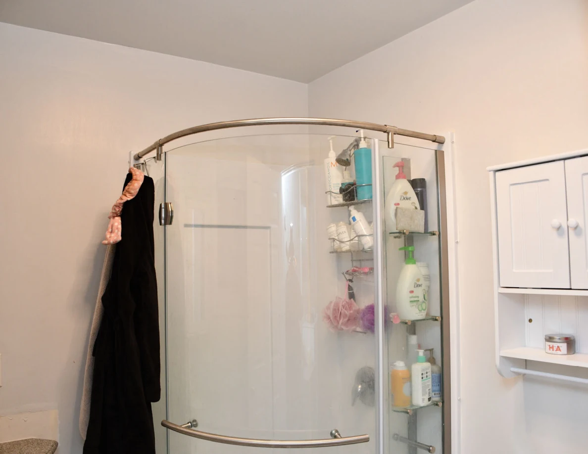 Curved shower enclosure with toiletries and hanging dark clothing.