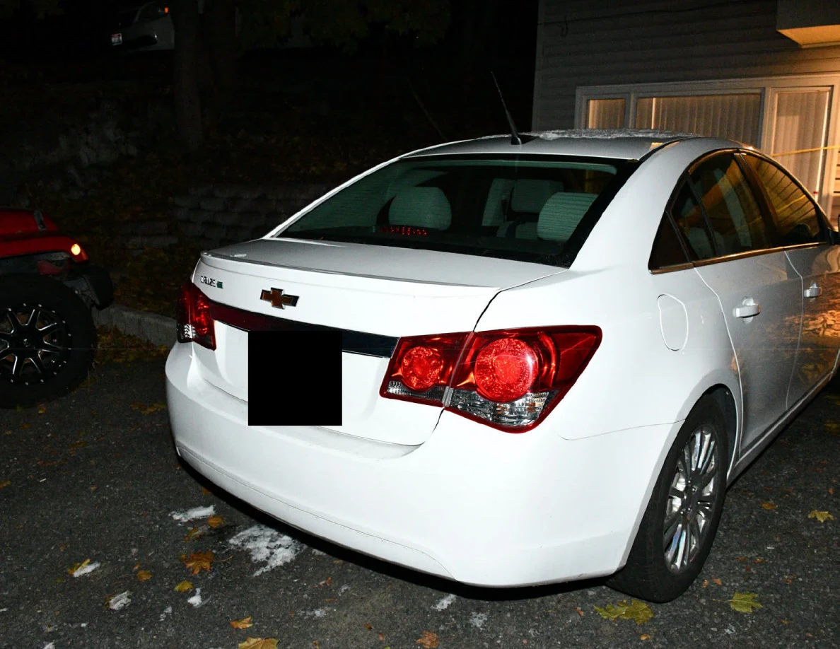Rear and side of a white Chevrolet sedan at night.