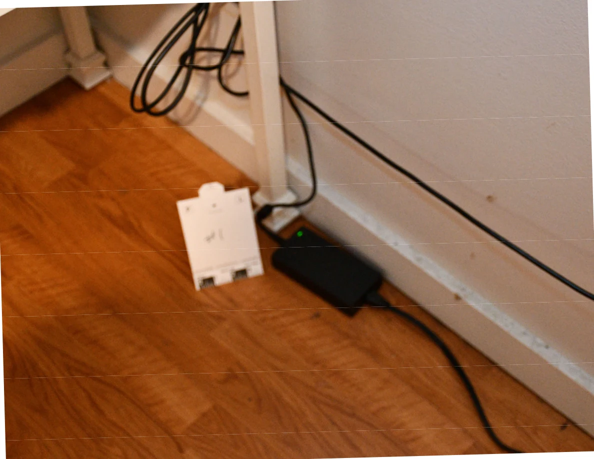 Small black electronic device and cables on wood floor beside a reference card.