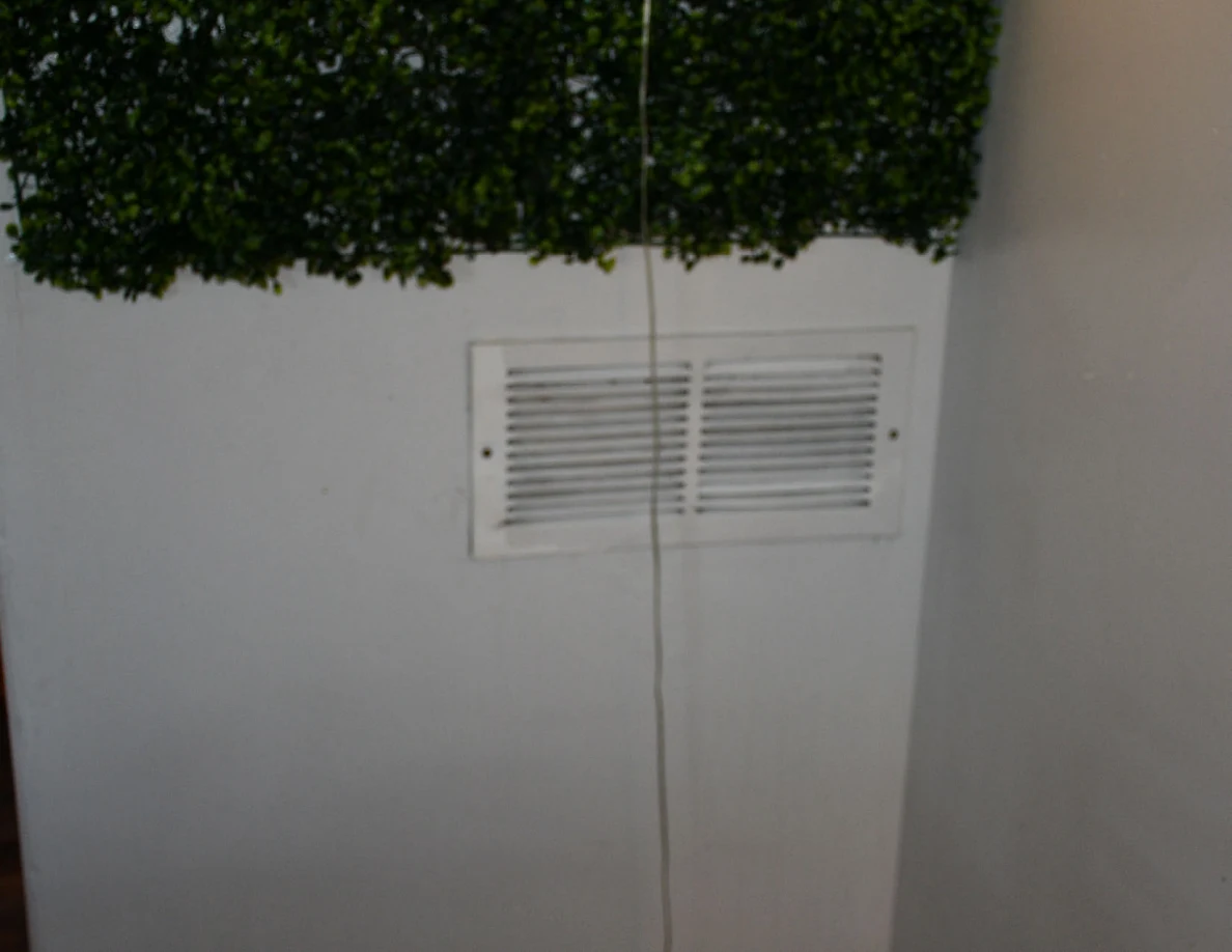 Wall air vent beneath decorative foliage panel.