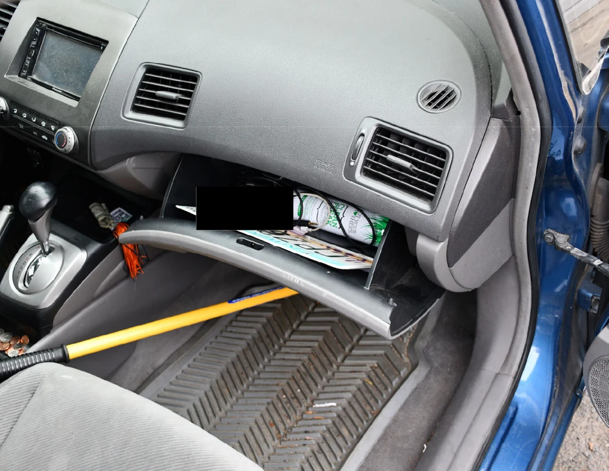 Car dashboard and open glove compartment with papers and a yellow-handled object below.