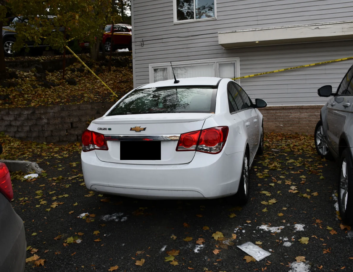 Rear of white Chevrolet sedan parked outside a house in daylight.