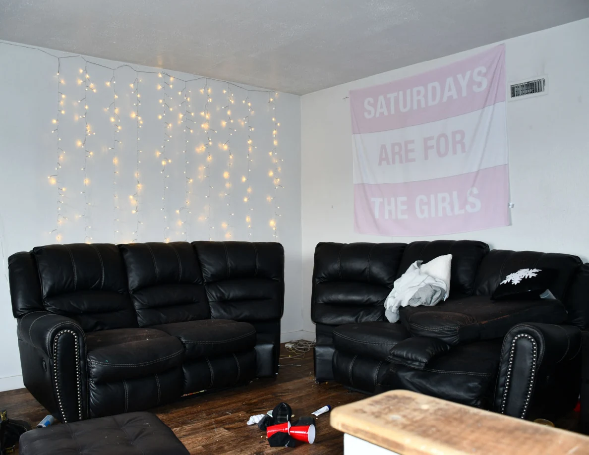 Black living-room sofas beneath string lights and wall banner.