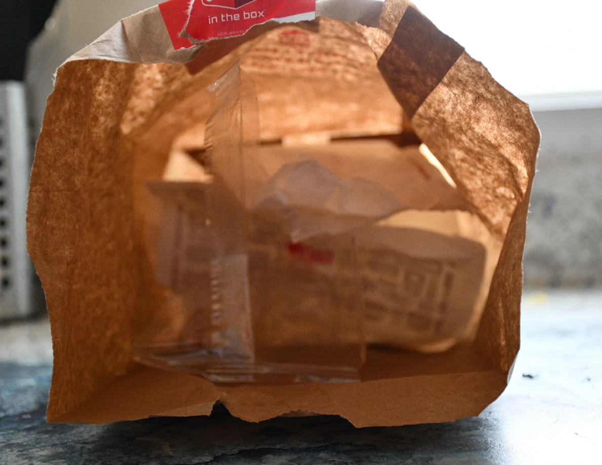 Close view inside an opened takeaway bag containing wrapped food packaging.