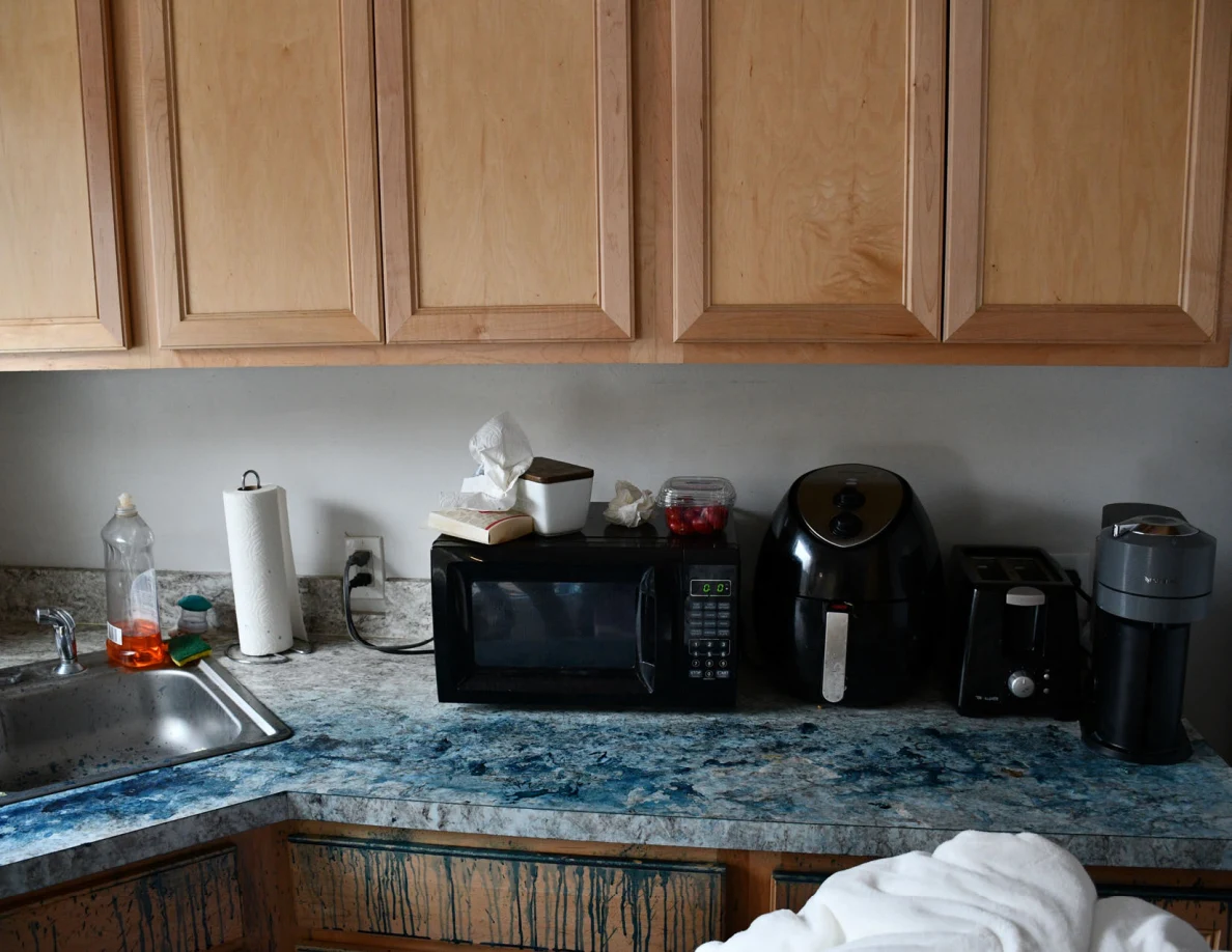 Kitchen countertop with sink, microwave, small appliances and wooden cabinets.