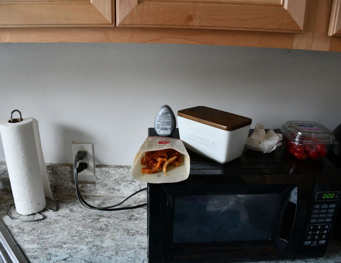 Microwave with food carton and butter container on top.