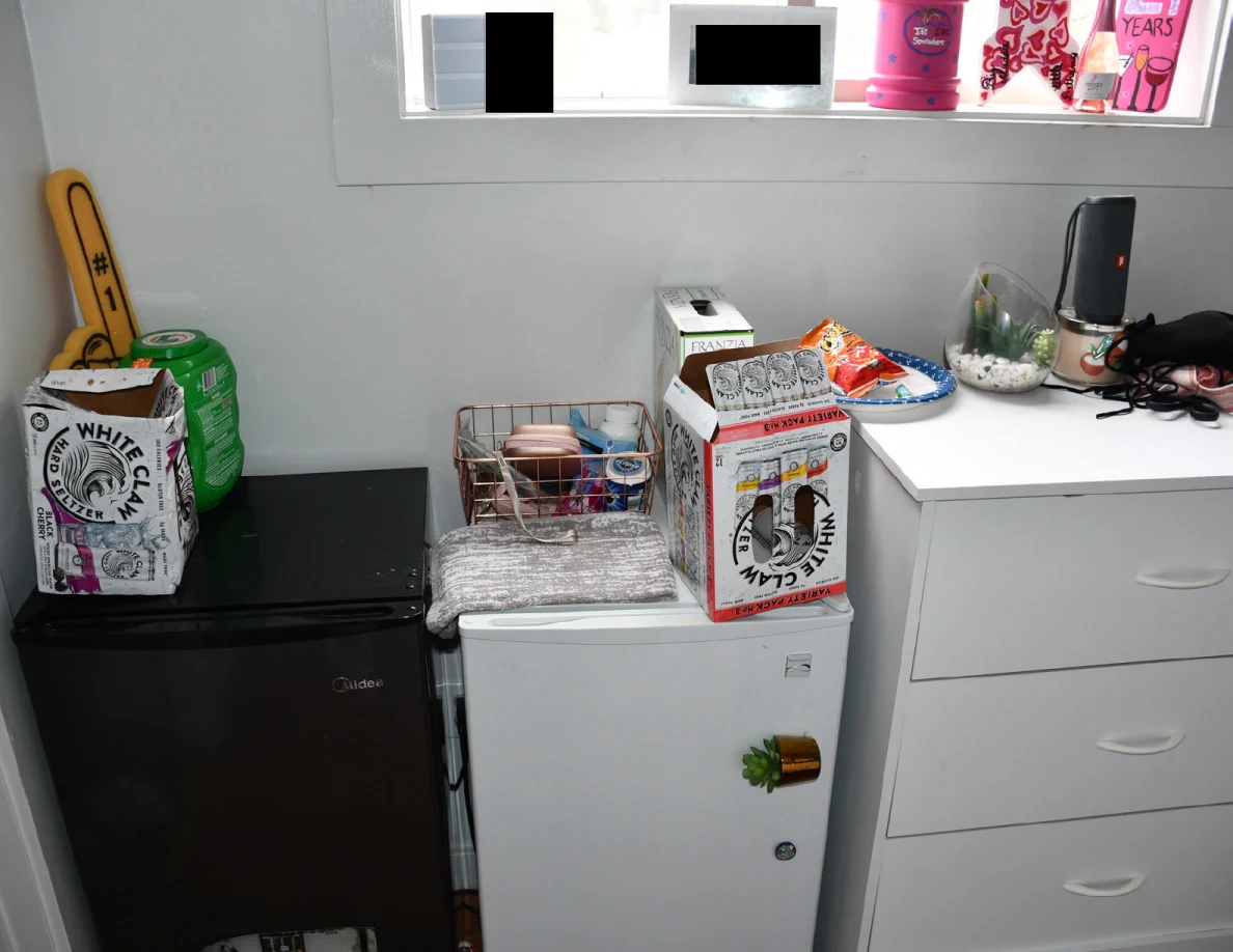 Compact refrigerators and drawers beneath window, with household items on top.