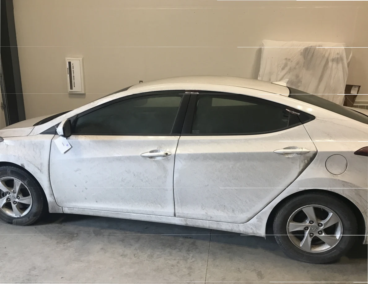 Side view of a dirty white sedan inside a garage or vehicle examination room.
