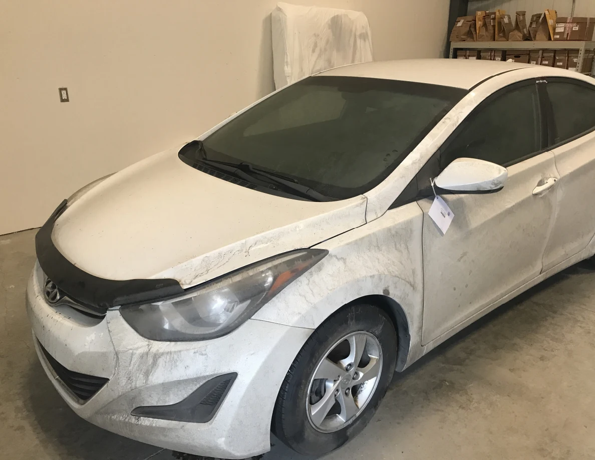 Front and side view of dirty white sedan indoors.