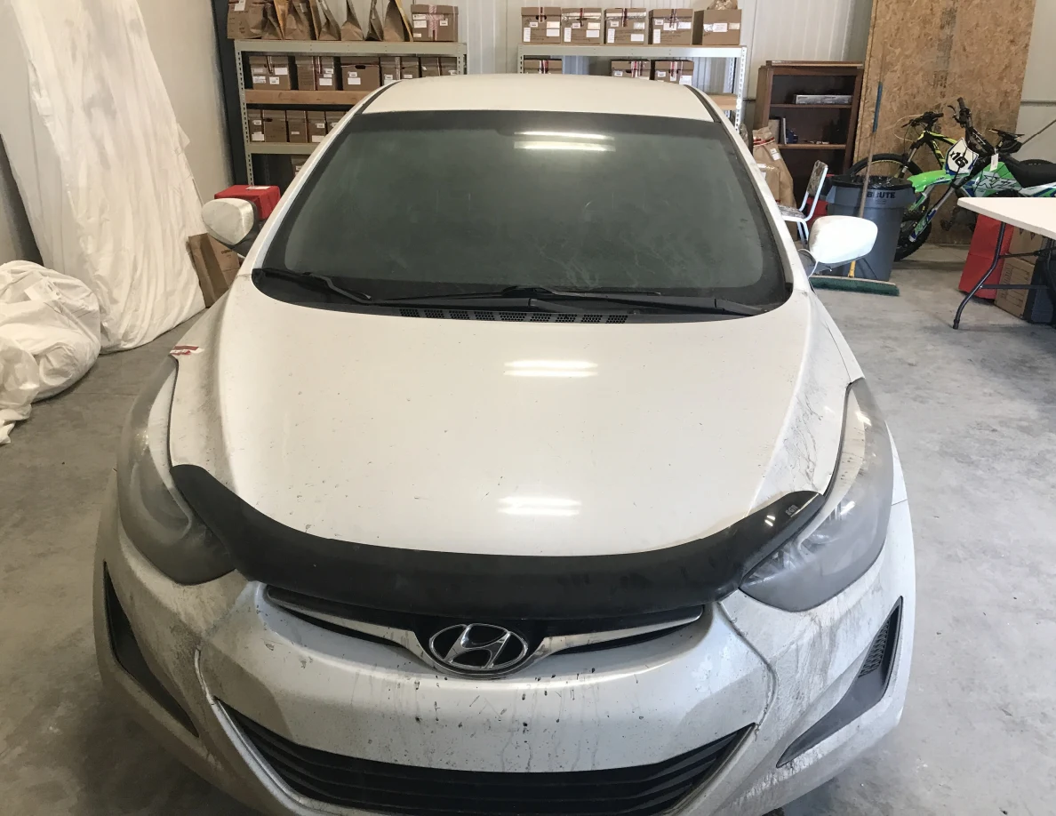 Front of white Hyundai sedan inside a garage with shelves behind.