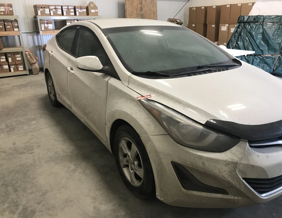 Front and side of white sedan with dirty exterior panels indoors.