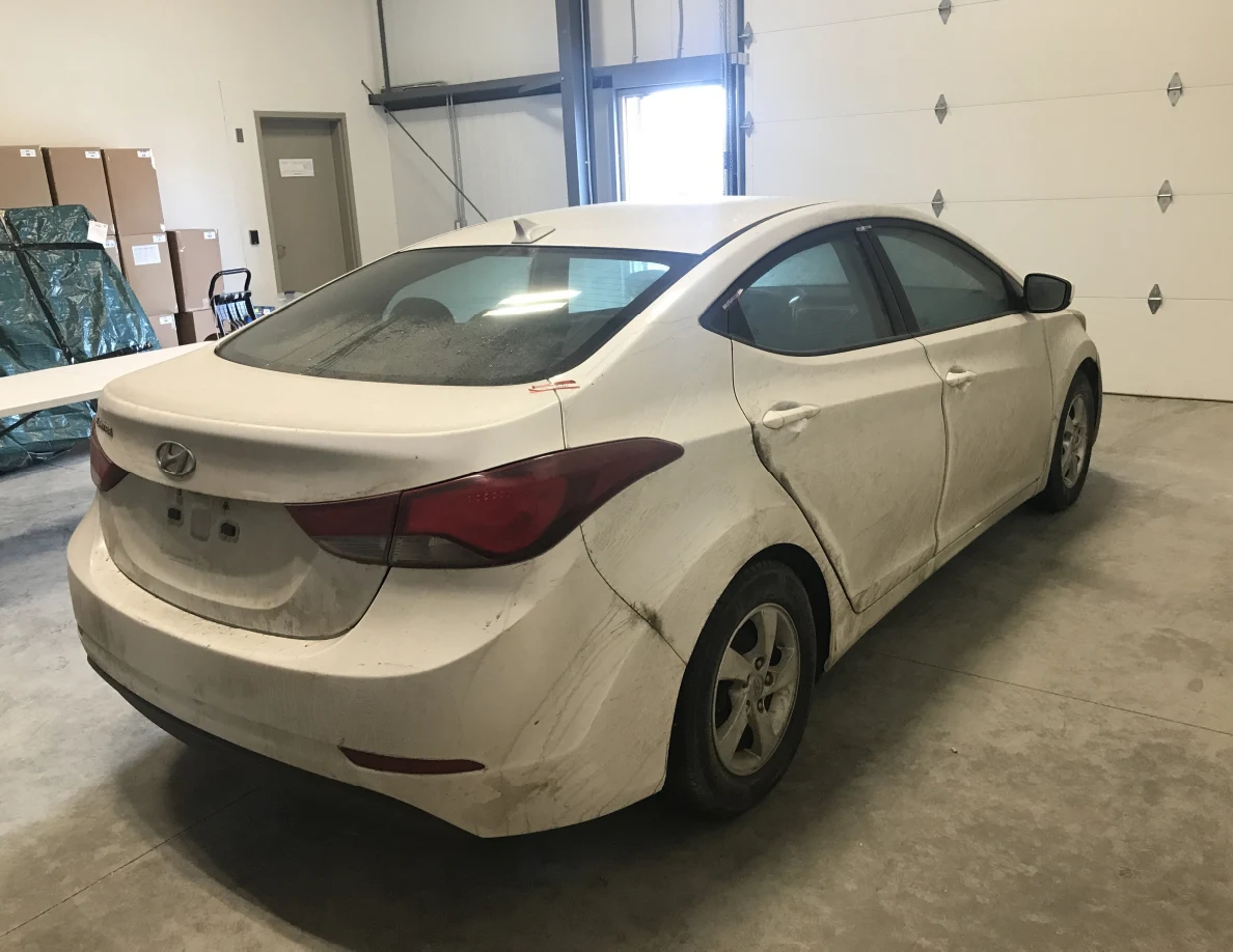 Rear and side of dirty white sedan near garage door.
