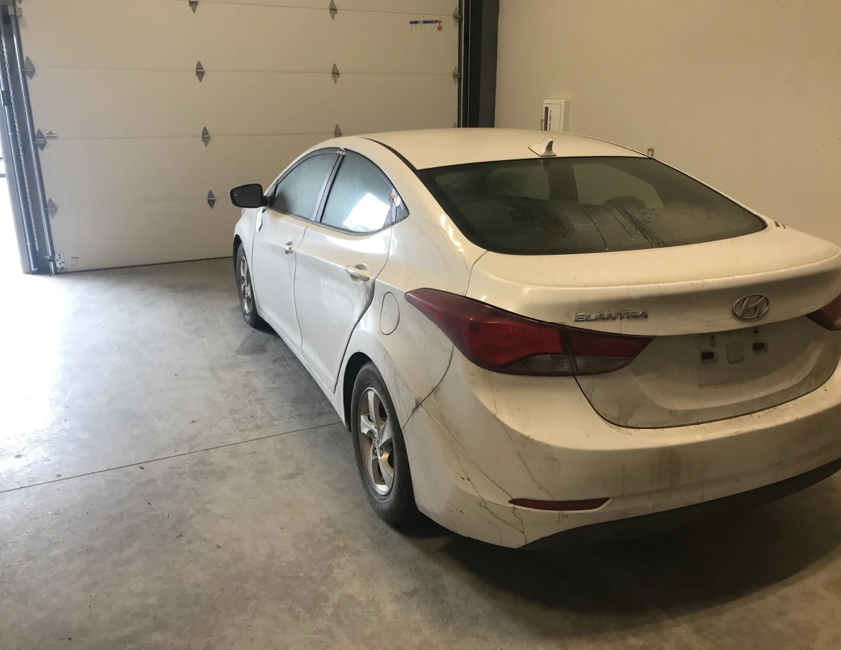 Rear quarter of white sedan near garage door.