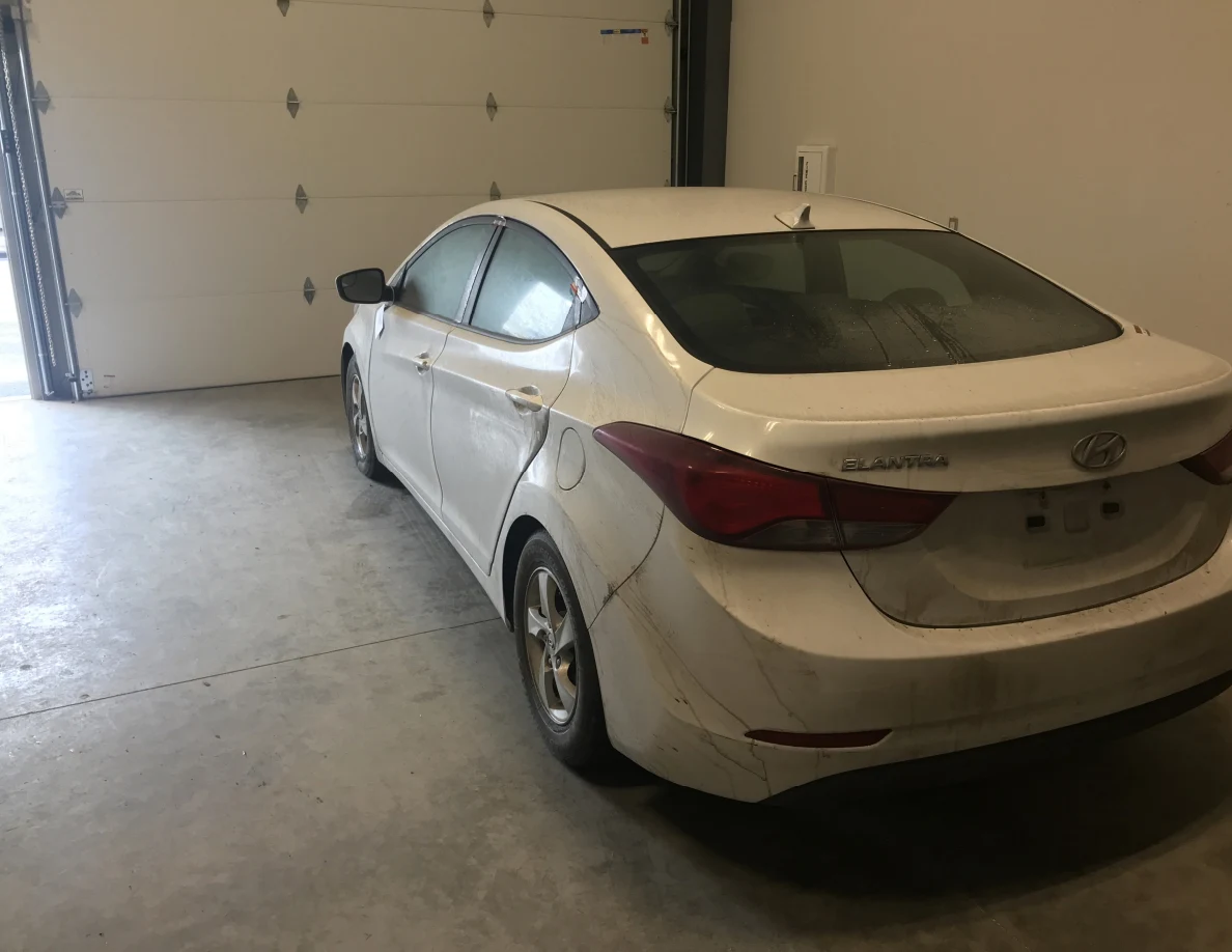 Rear and side view of white sedan inside garage.