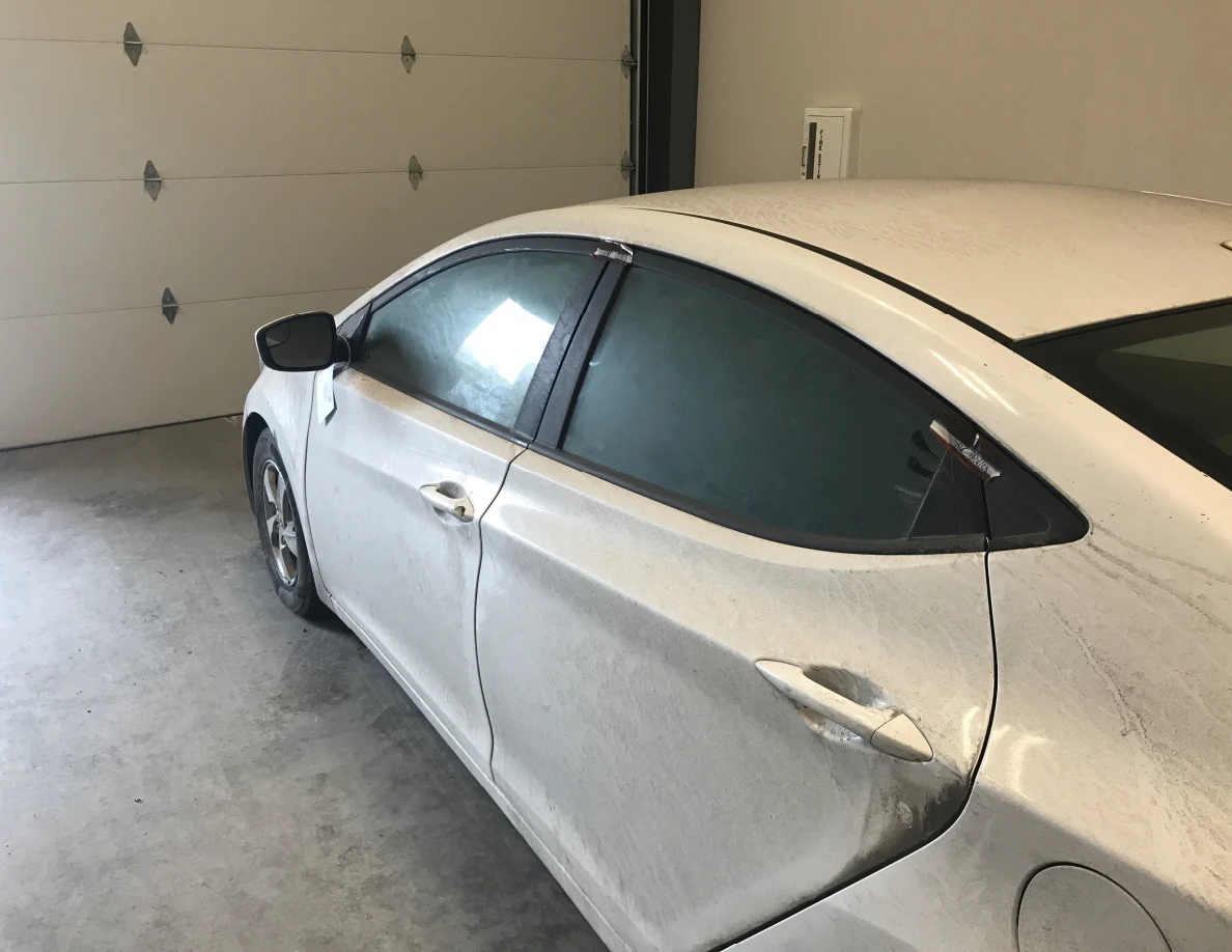 Side windows and rear door of dirty white sedan.